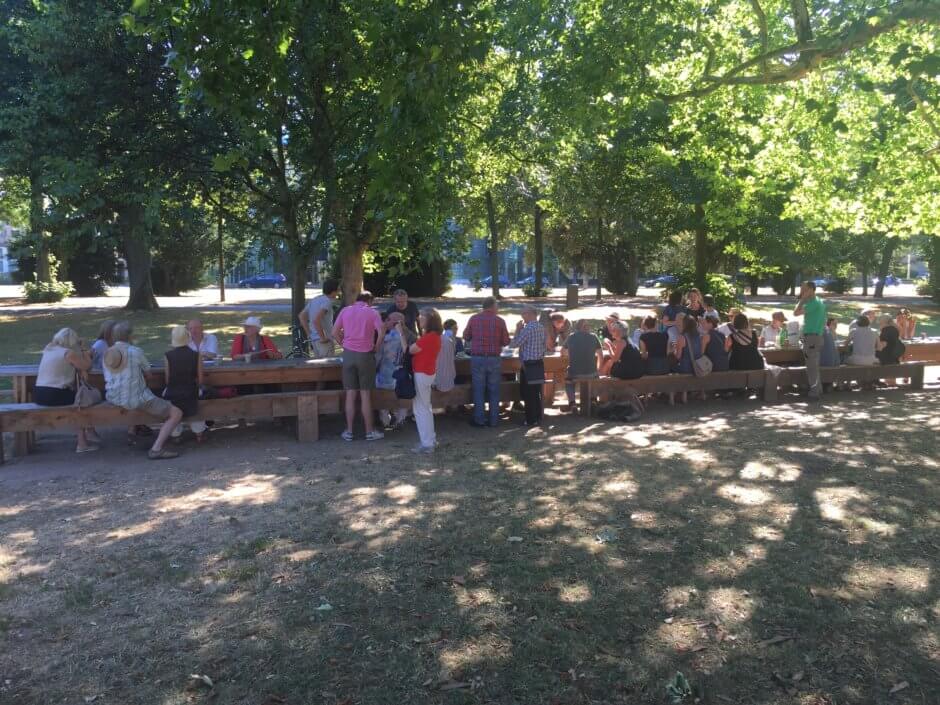 Langer Tisch im kleinen Park Sachsenring vor dem Humboldt; Menschen am Tisch